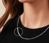 Silver necklace with a circular pendant worn by a person against a neutral background