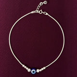 payal with a blue evil eye bead on a purple background
