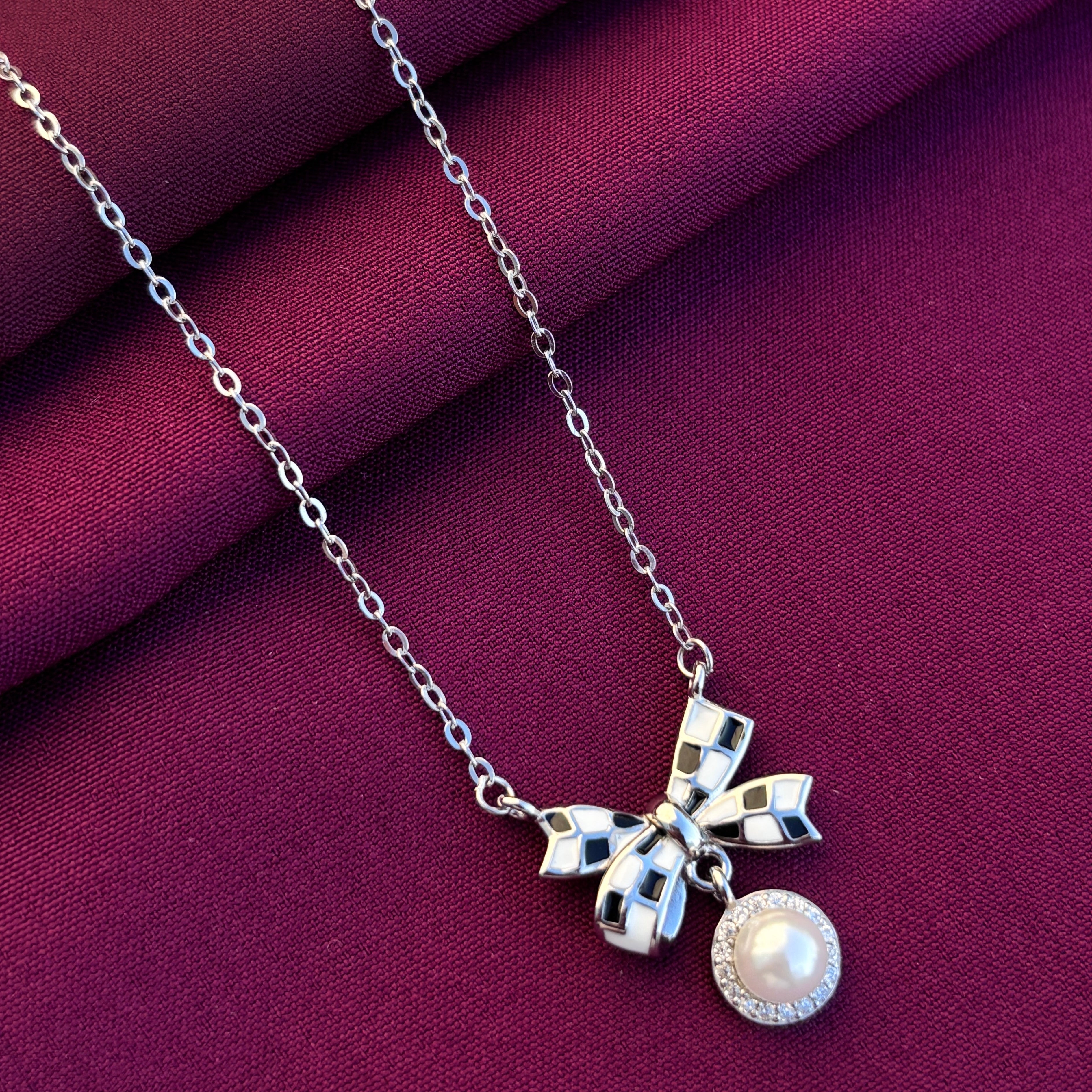 Silver necklace with a bow and pearl pendant on a purple fabric background