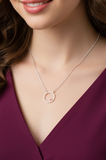 Necklace with a circular pendant worn by a person in a purple top