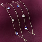 silver payal with blue evil eye charms on a purple background