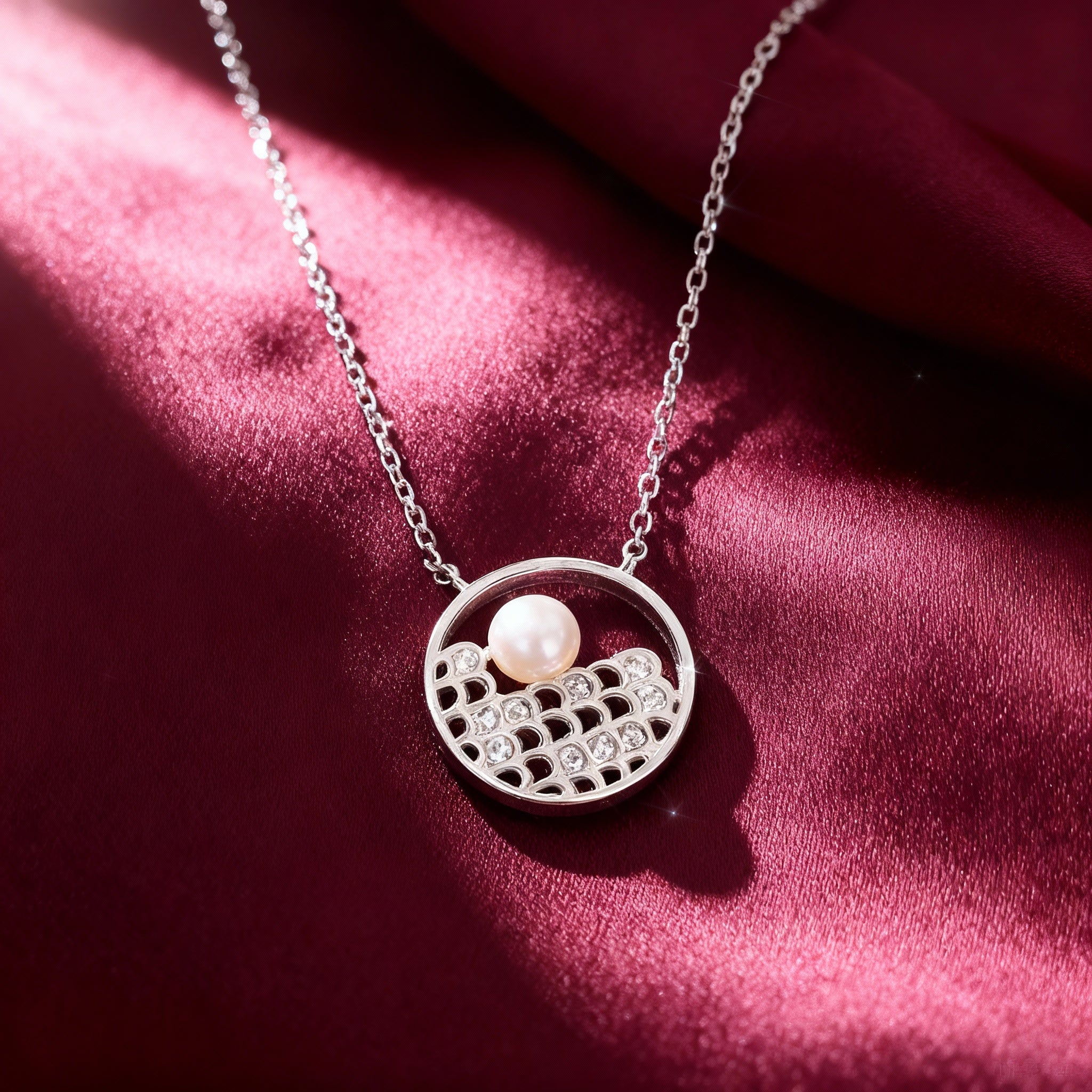 Silver necklace with a pendant featuring a pearl on a red fabric background