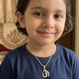 Child wearing a silver pendent with an Om symbol in a home setting