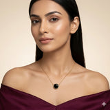 Woman wearing a gold necklace with a black pendant against a beige background