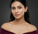 Woman wearing a silver necklace with a heart pendant against a dark background