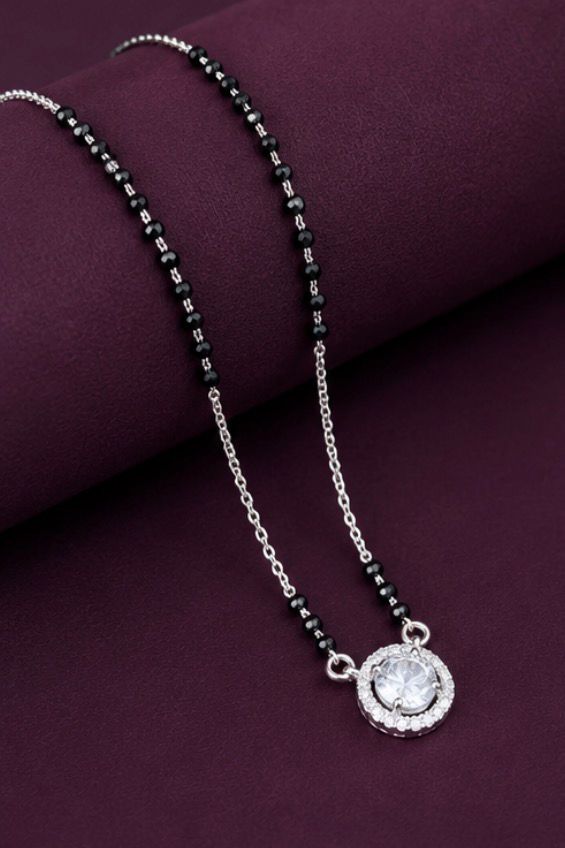 Necklace with black beads and a silver pendant on a purple surface