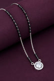 Necklace with black beads and a silver pendant on a purple surface