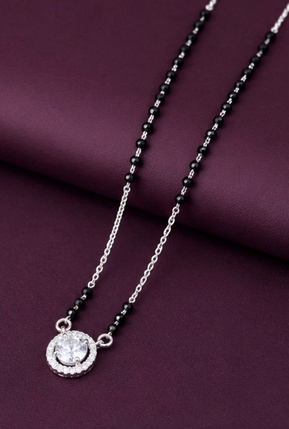 Necklace with black beads and a silver pendant on a purple fabric background