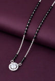 Necklace with black beads and a silver pendant on a purple fabric background