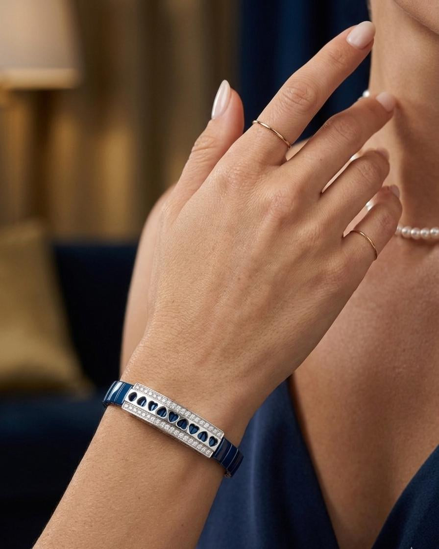 Close-up of a person's hand wearing a blue bracelet with heart patterns, with a blurred indoor background.