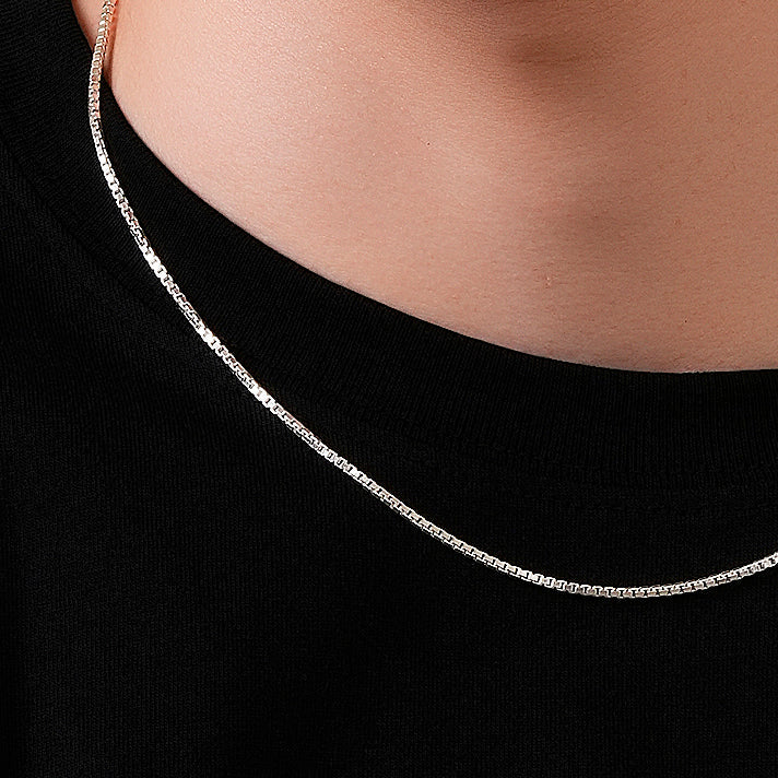 Silver chain necklace worn by a person on a black background