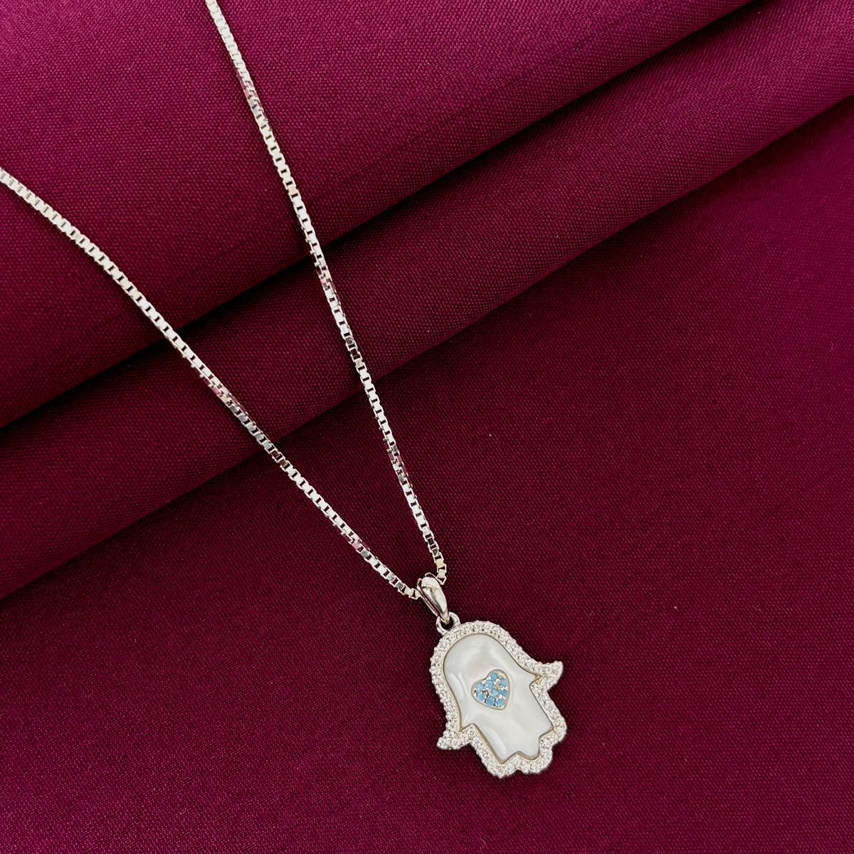 Silver necklace with a hamsa hand pendant on a red fabric background