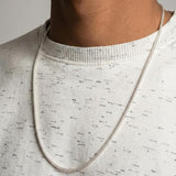 Person wearing a silver chain necklace on a plain background