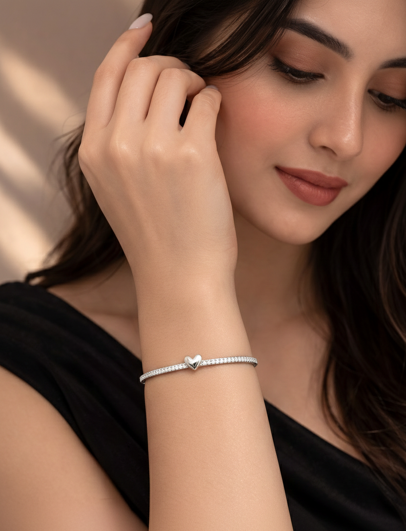 Woman wearing a silver bracelet with a heart charm, against a neutral background