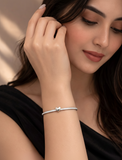 Woman wearing a silver bracelet with a heart charm, against a neutral background