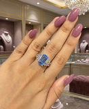 Hand wearing a ring with a blue gemstone in a jewelry store setting