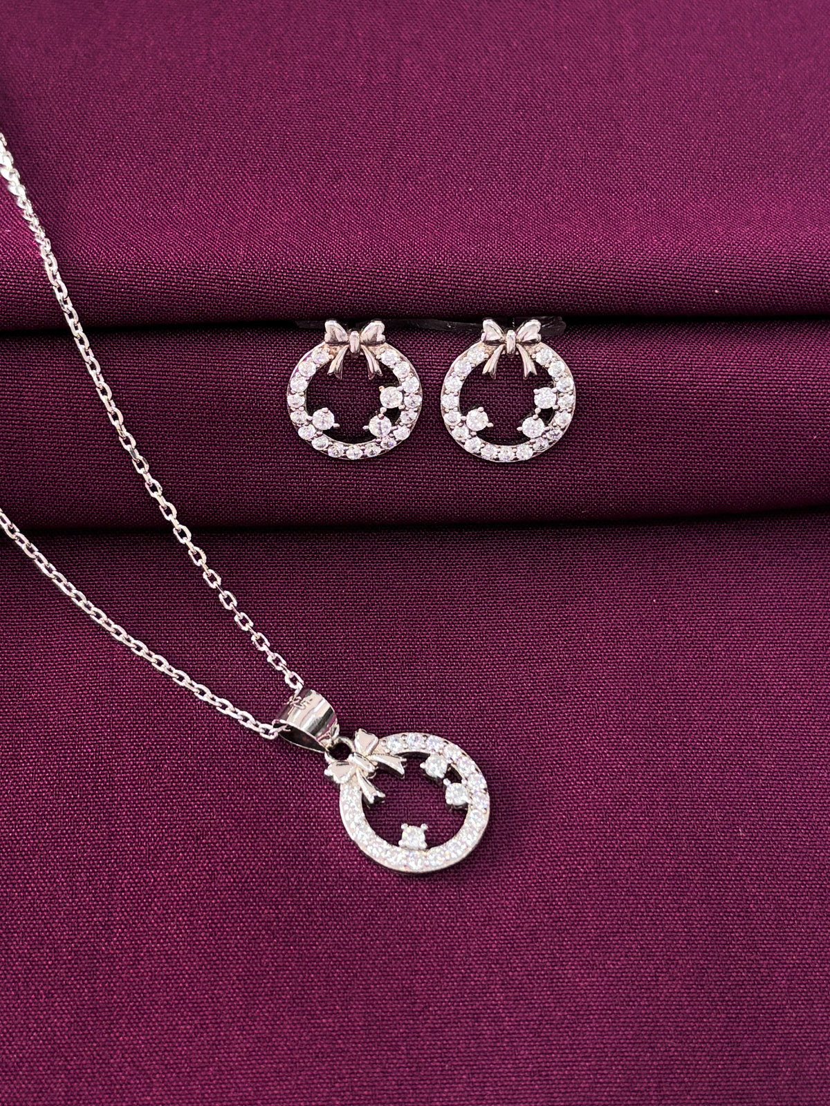 Silver necklace and earrings set on a purple fabric background