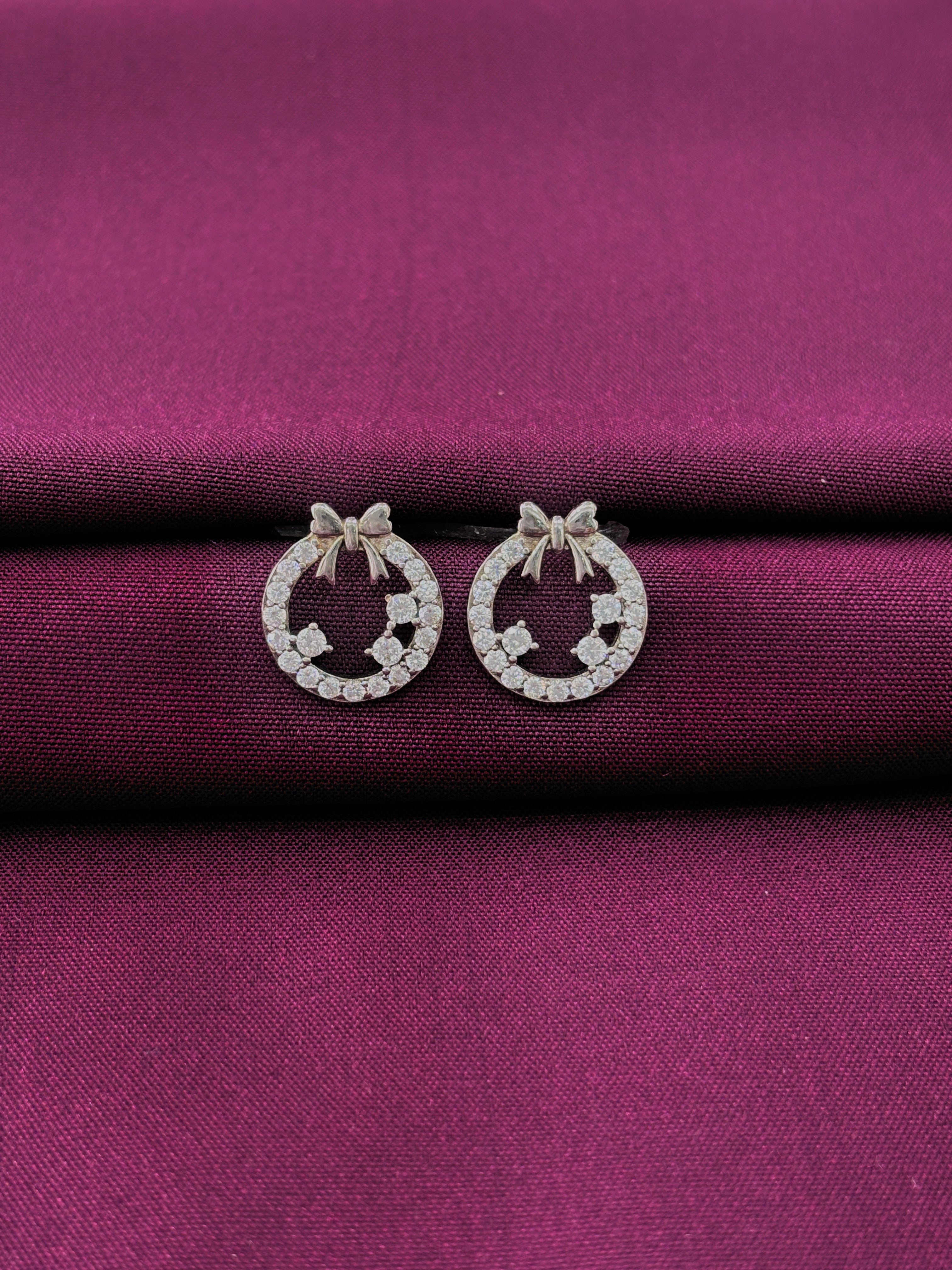 Silver round bow earrings with clear stones on a purple fabric background