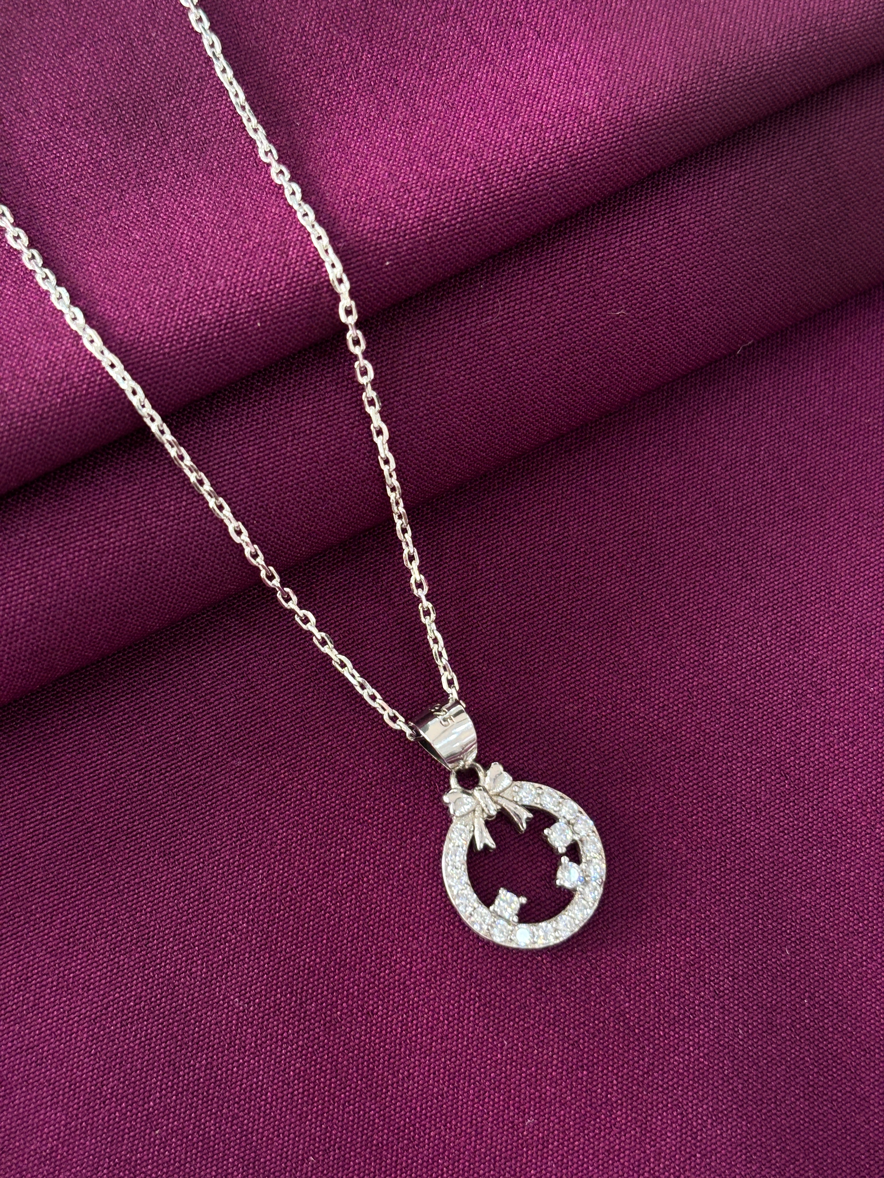 Silver necklace with a bow round-shaped pendant on a purple fabric background