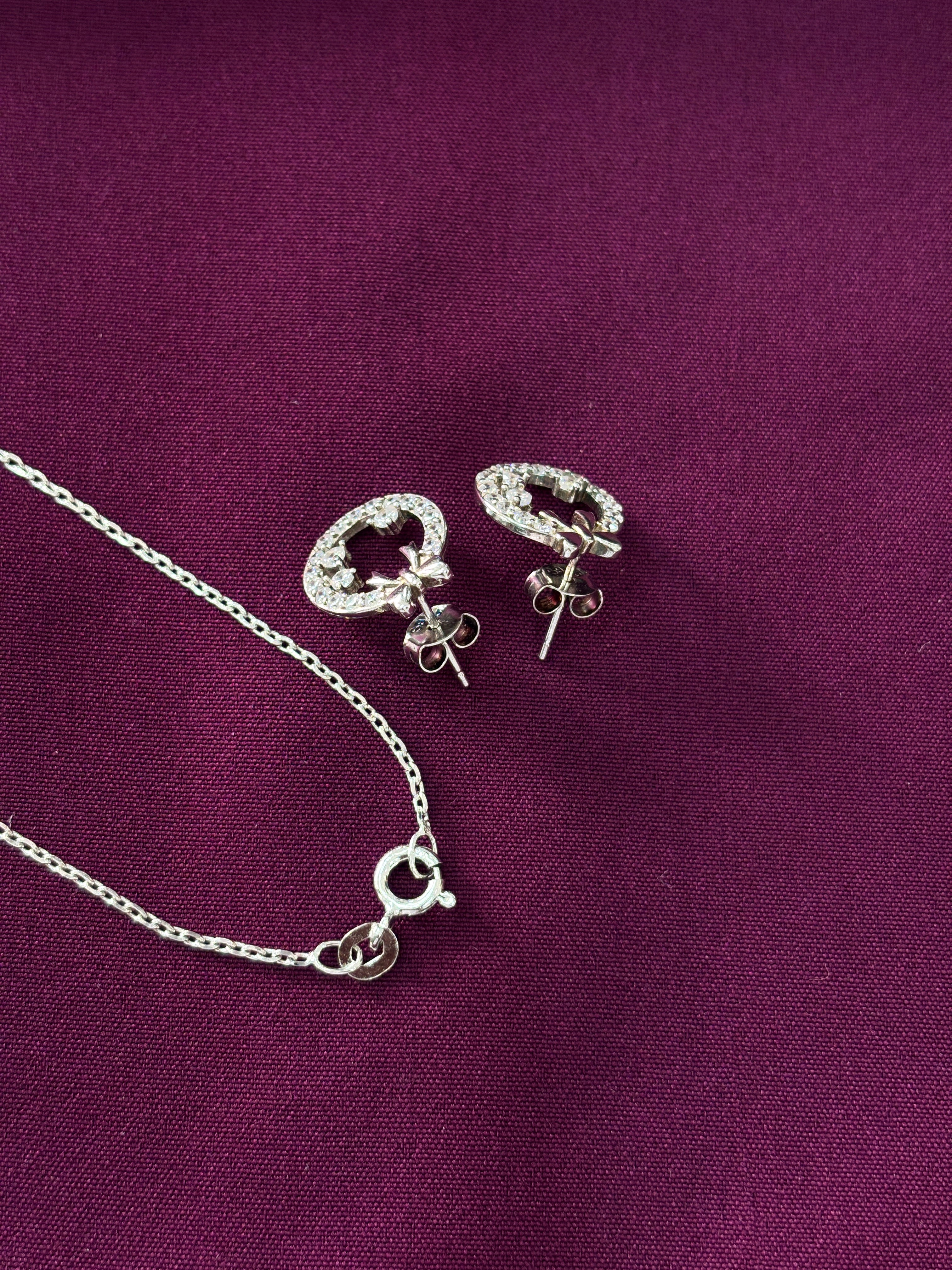 Silver jewelry set with bow round-shaped pendants on a purple fabric background