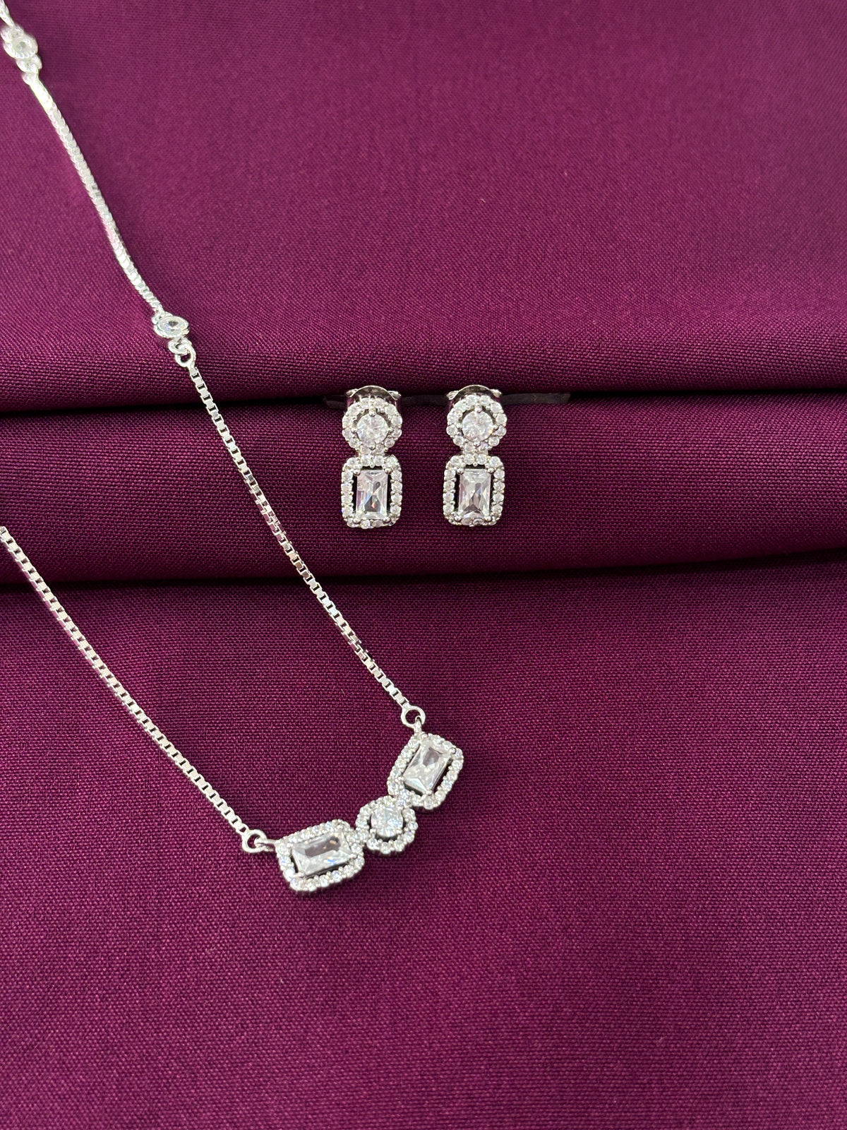 Silver jewelry set with necklace and earrings on a purple fabric background