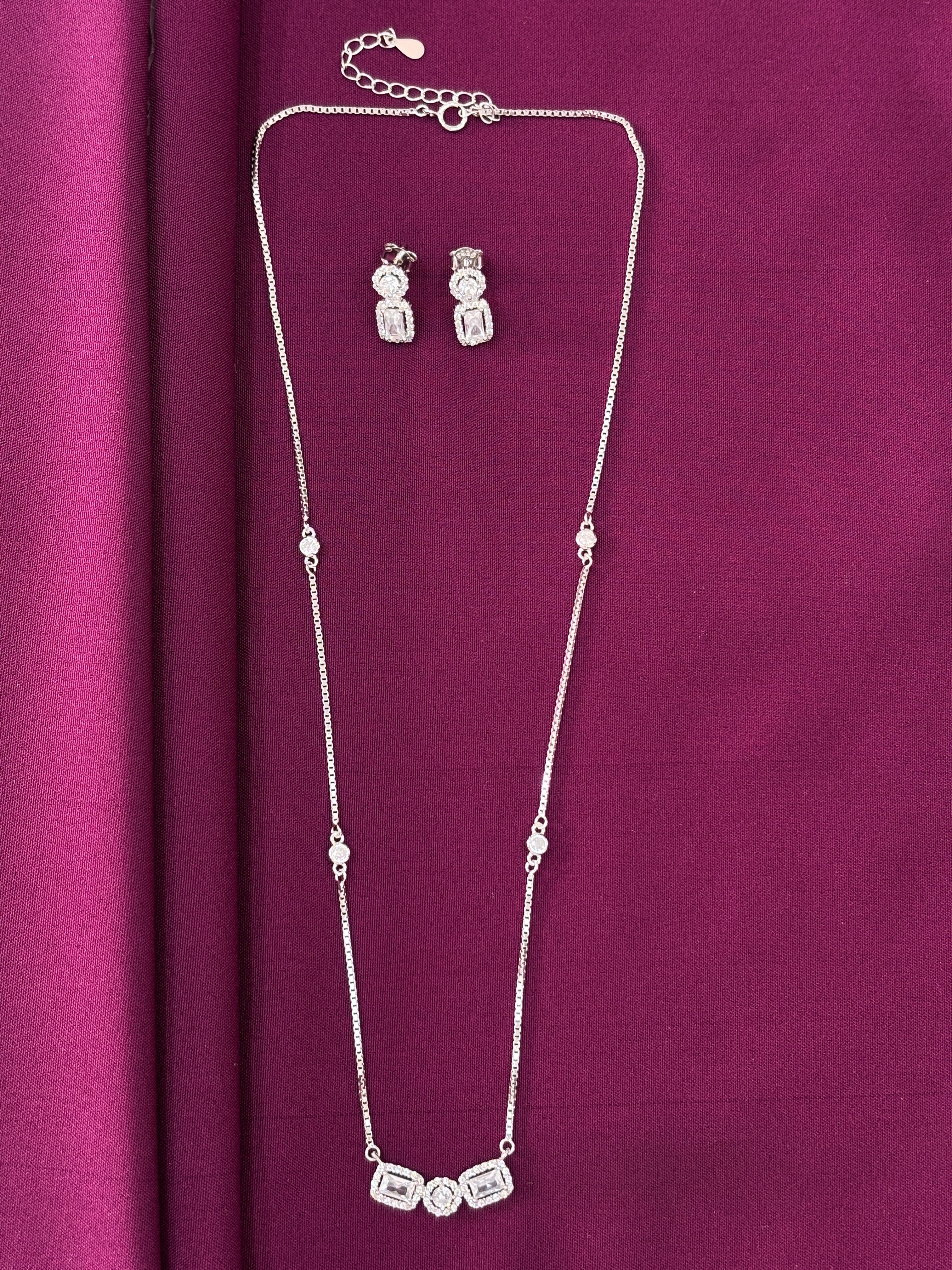 Silver necklace and earrings on a purple fabric background