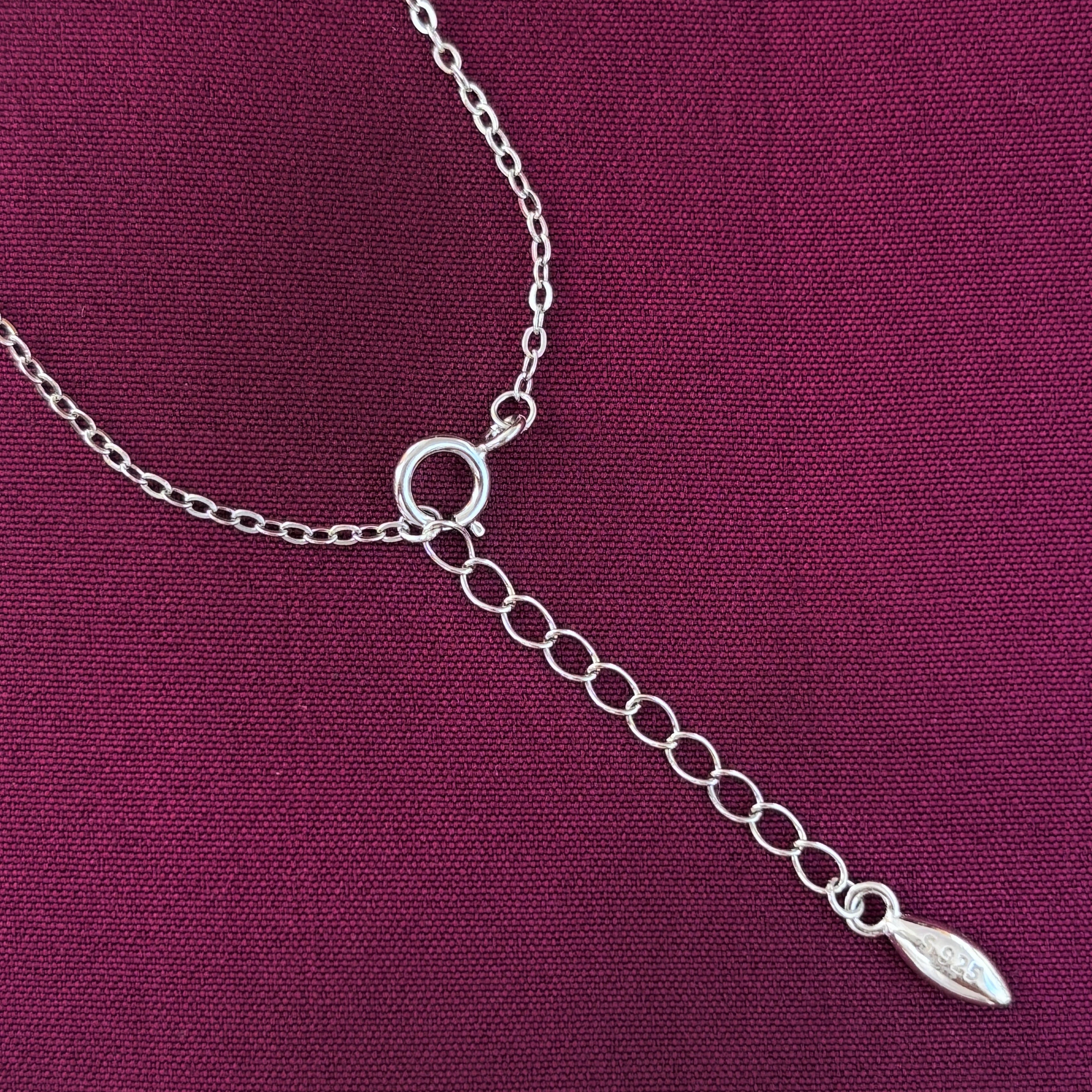 Silver chain necklace with a leaf-shaped pendant on a purple fabric background
