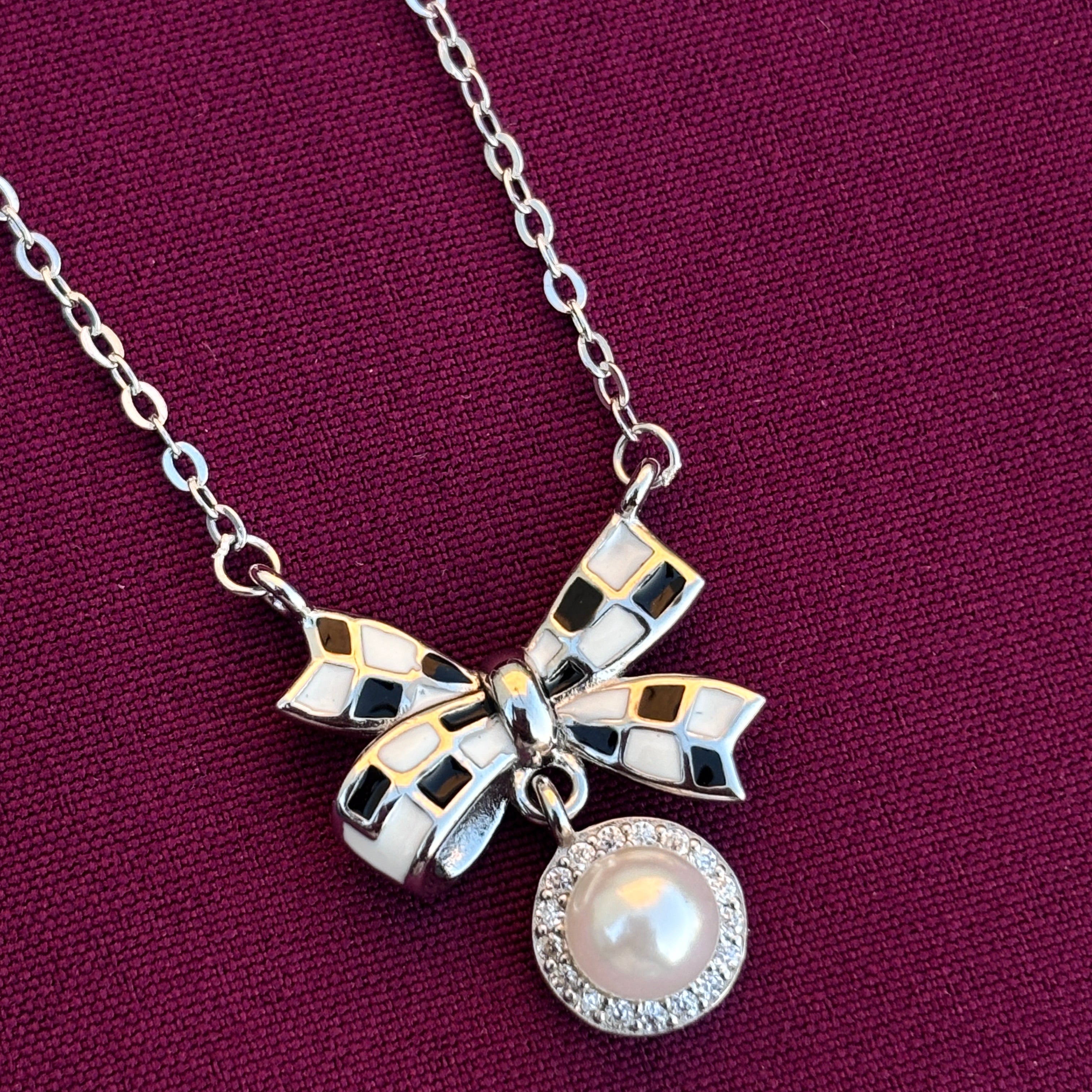 Necklace with a silver bow and pearl charm on a purple background