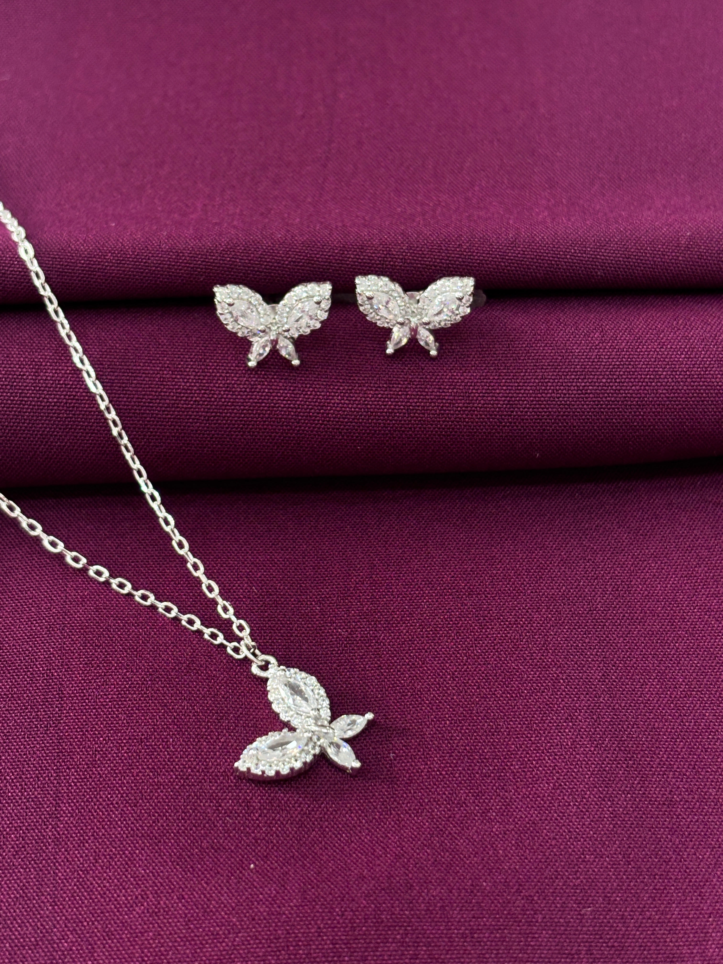 Butterfly-shaped silver earrings on a purple fabric background