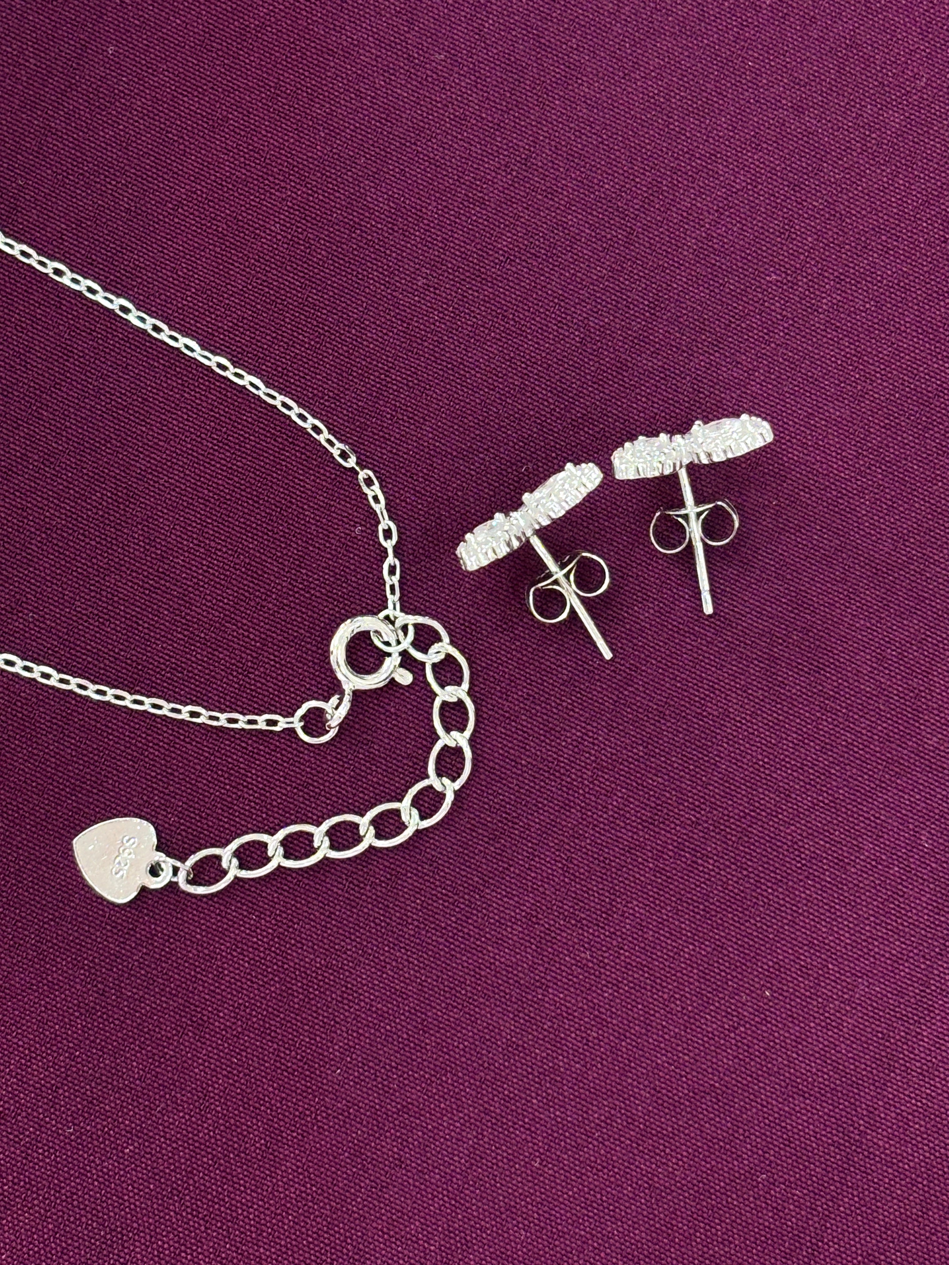 Silver jewelry set including necklace and earrings on a purple fabric background