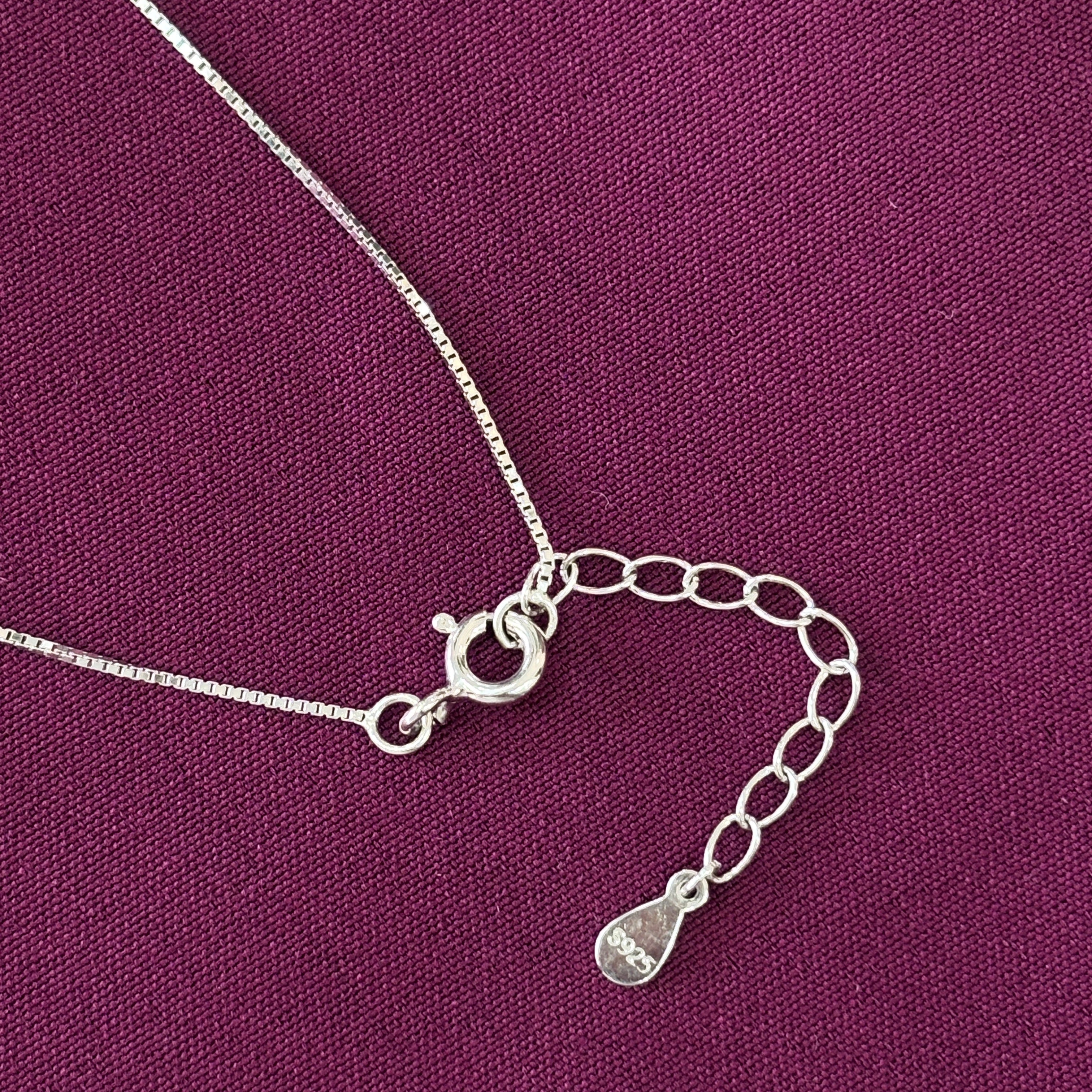 Close-up of a silver necklace clasp on a purple fabric background