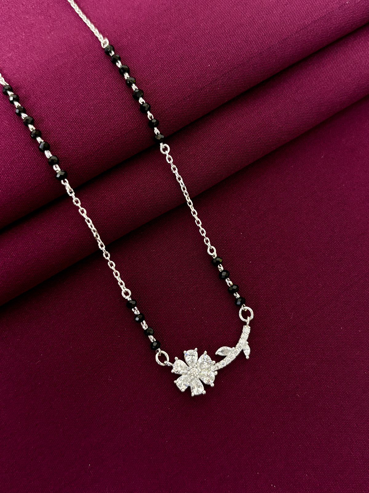 Silver mangalsutra with a floral pendant on a purple fabric background