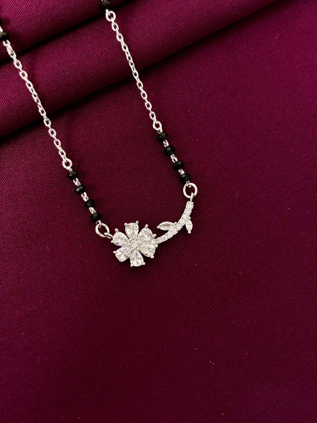 mangalsutra with a floral pendant on a maroon fabric background