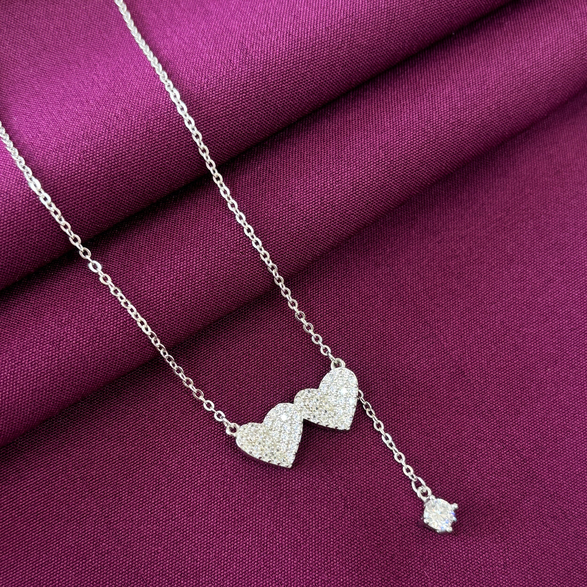 Silver necklace with a dual heart pendant on a purple fabric background