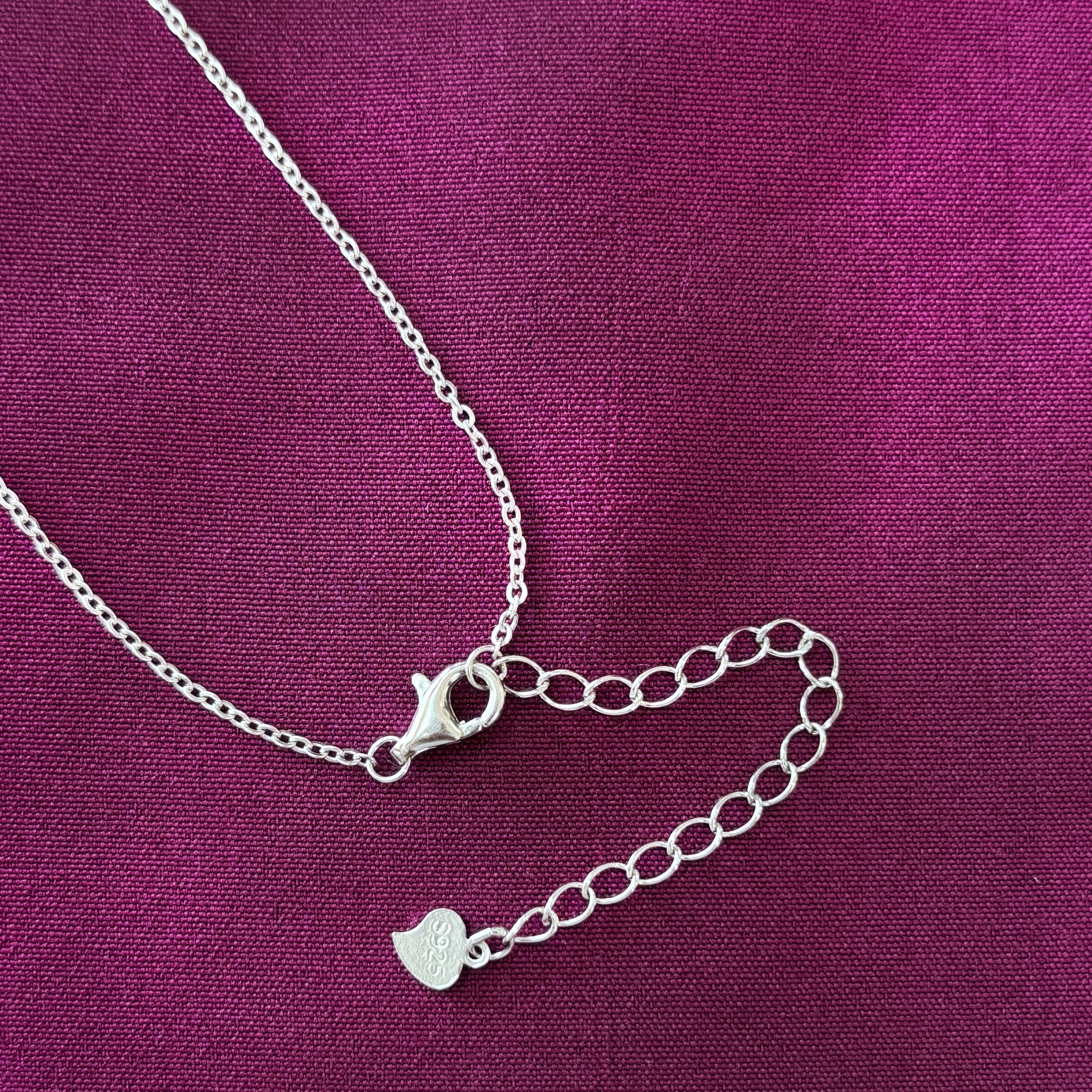 Silver bracelet with a heart charm on a purple fabric background