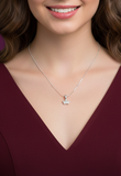 Silver necklace with a crown pendant worn by a person in a burgundy top.