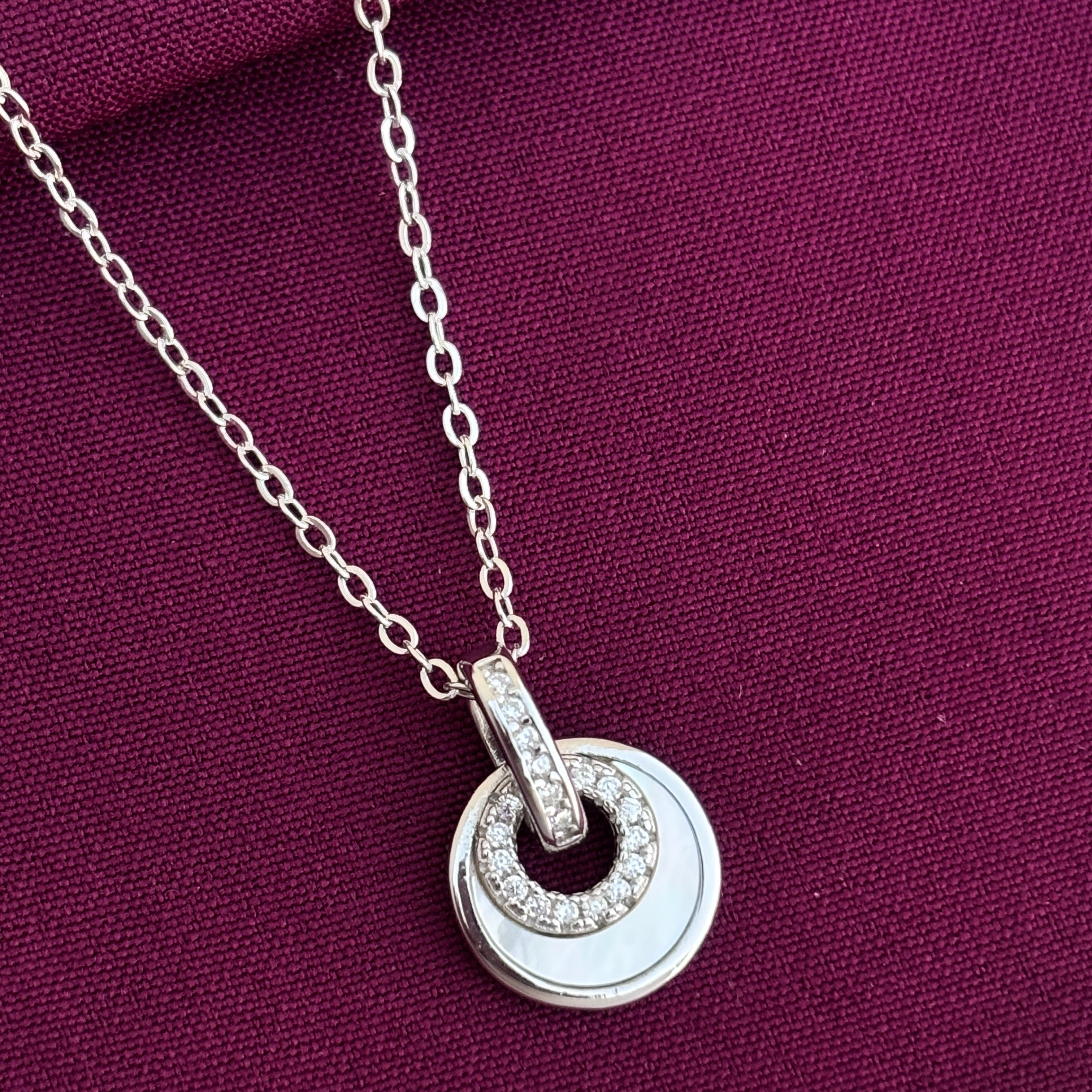 Silver necklace with a circular pendant on a purple fabric background