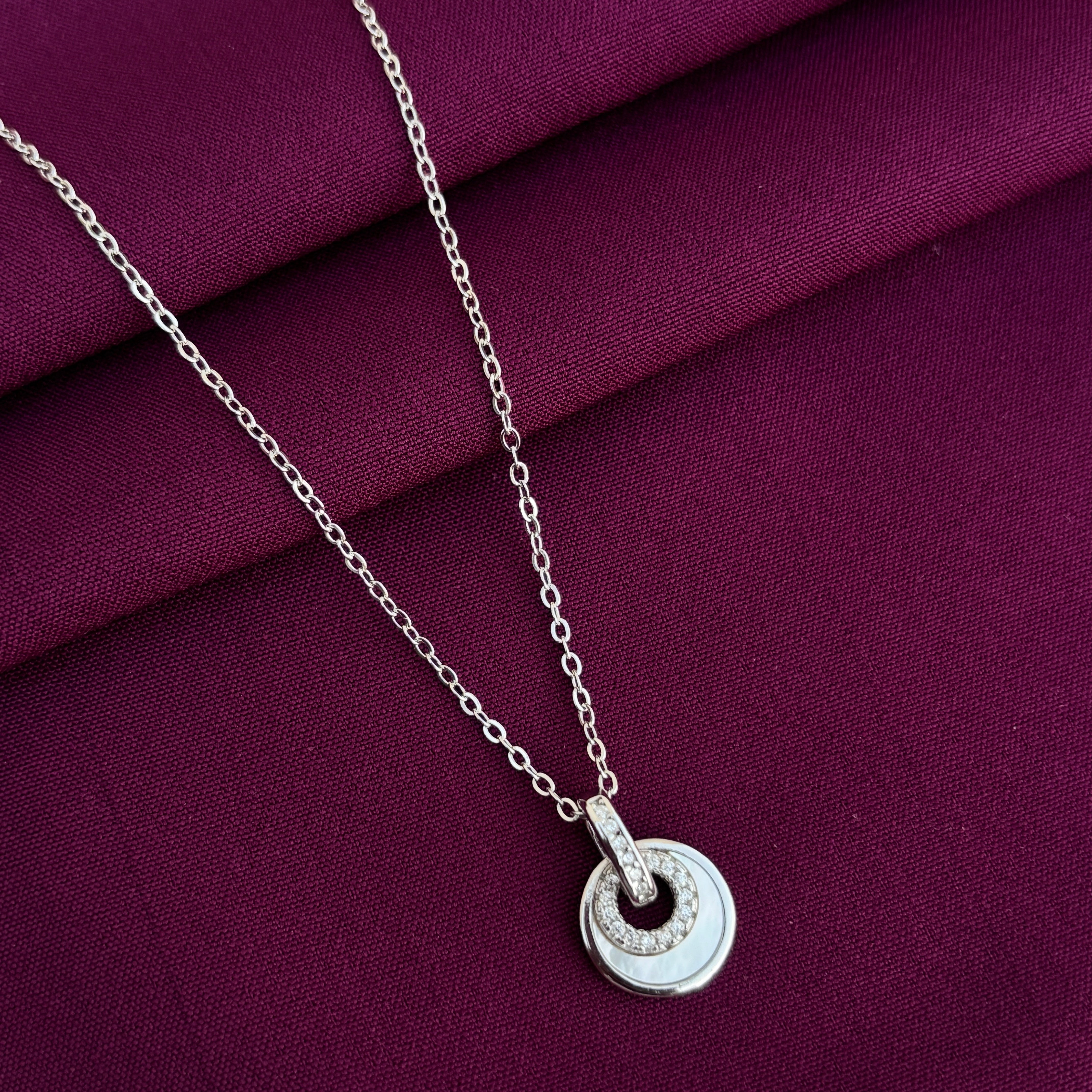 Silver necklace with a circular pendant on a purple fabric background