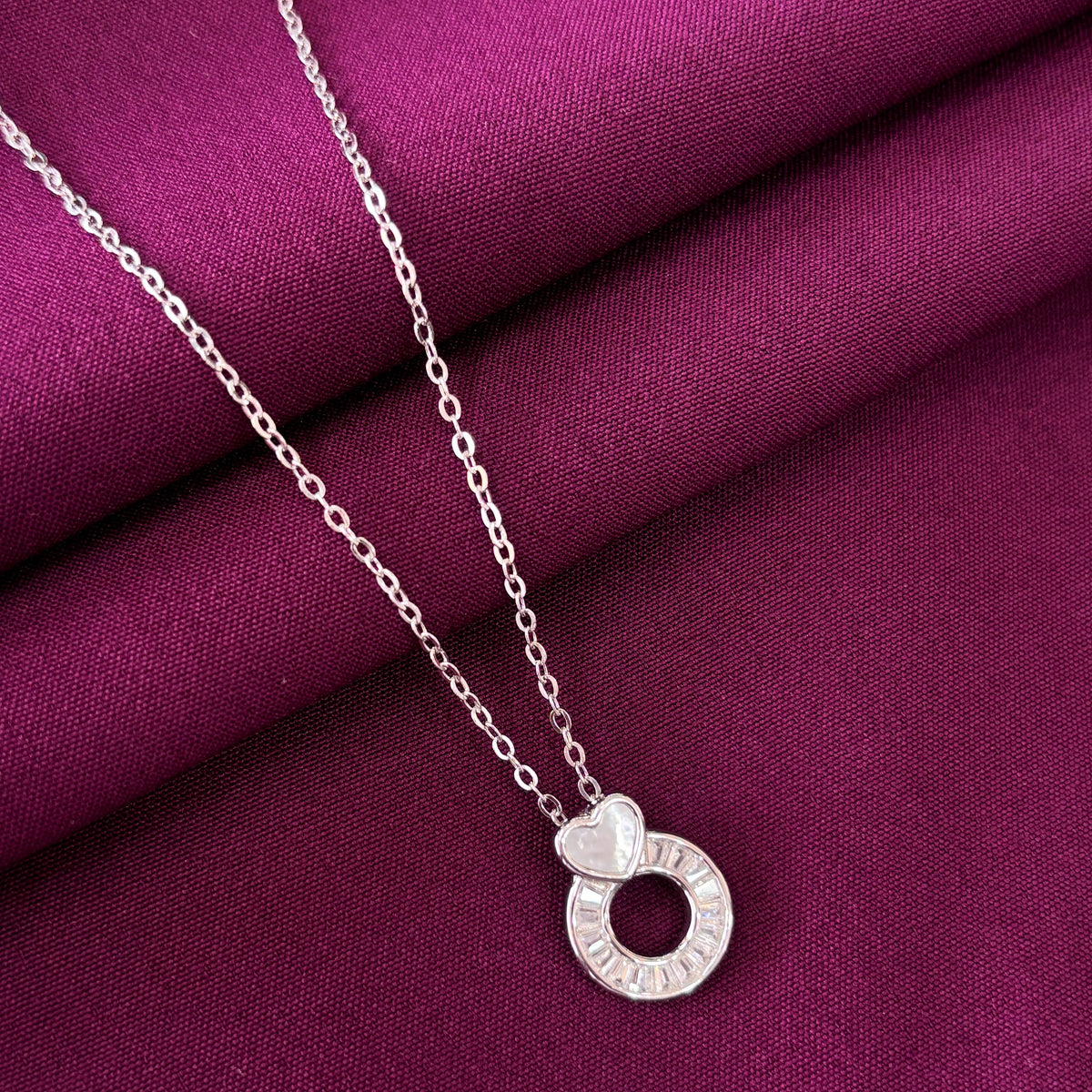 Silver necklace with a circular pendant on a purple fabric background