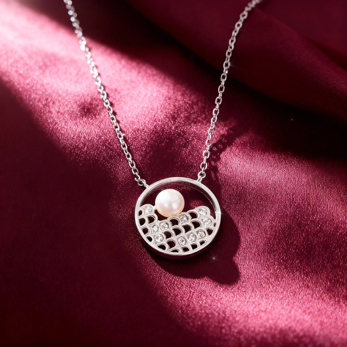Silver necklace with a pendant featuring a pearl on a red fabric background