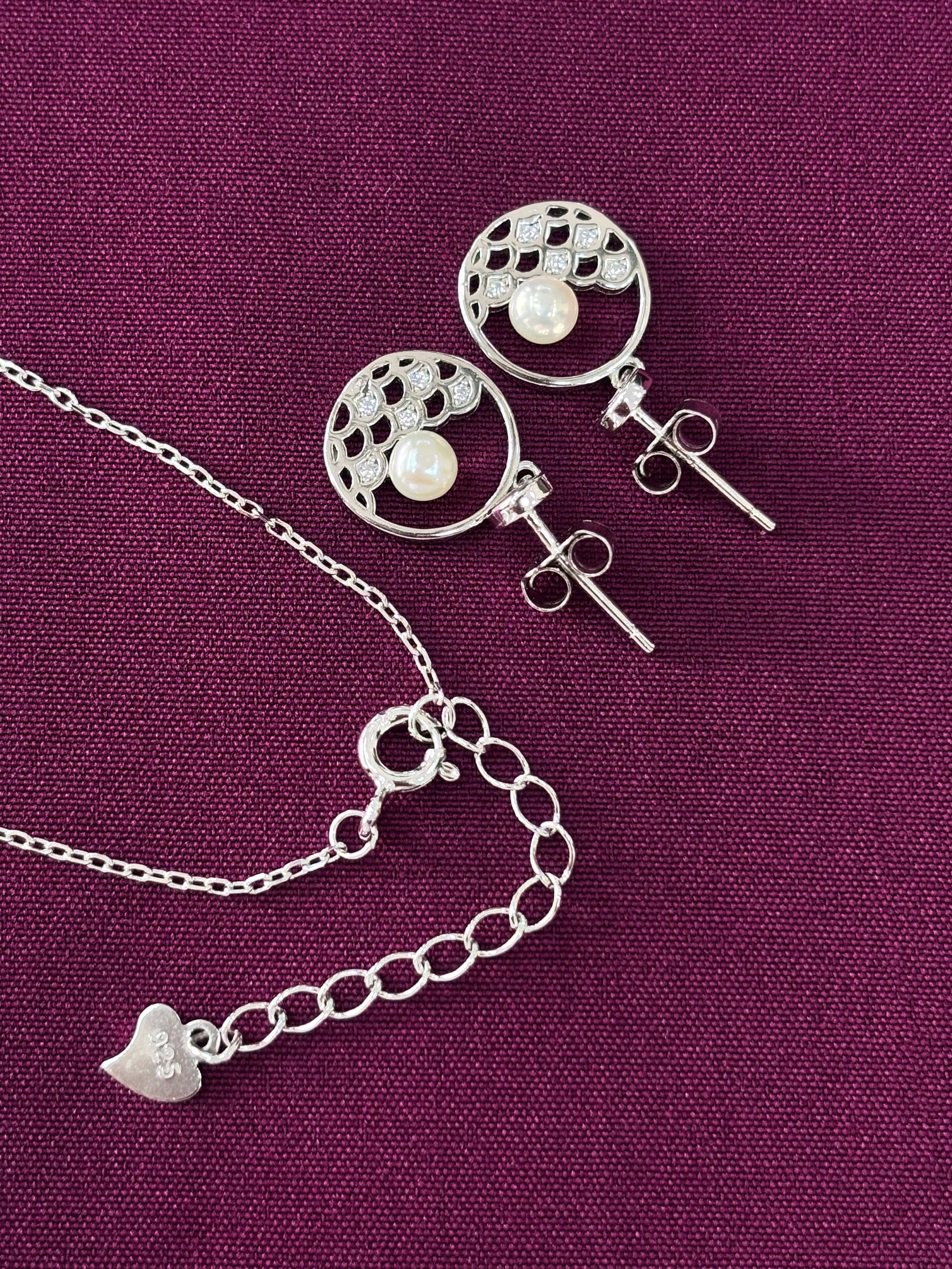 Silver earrings and necklace set on a purple fabric background