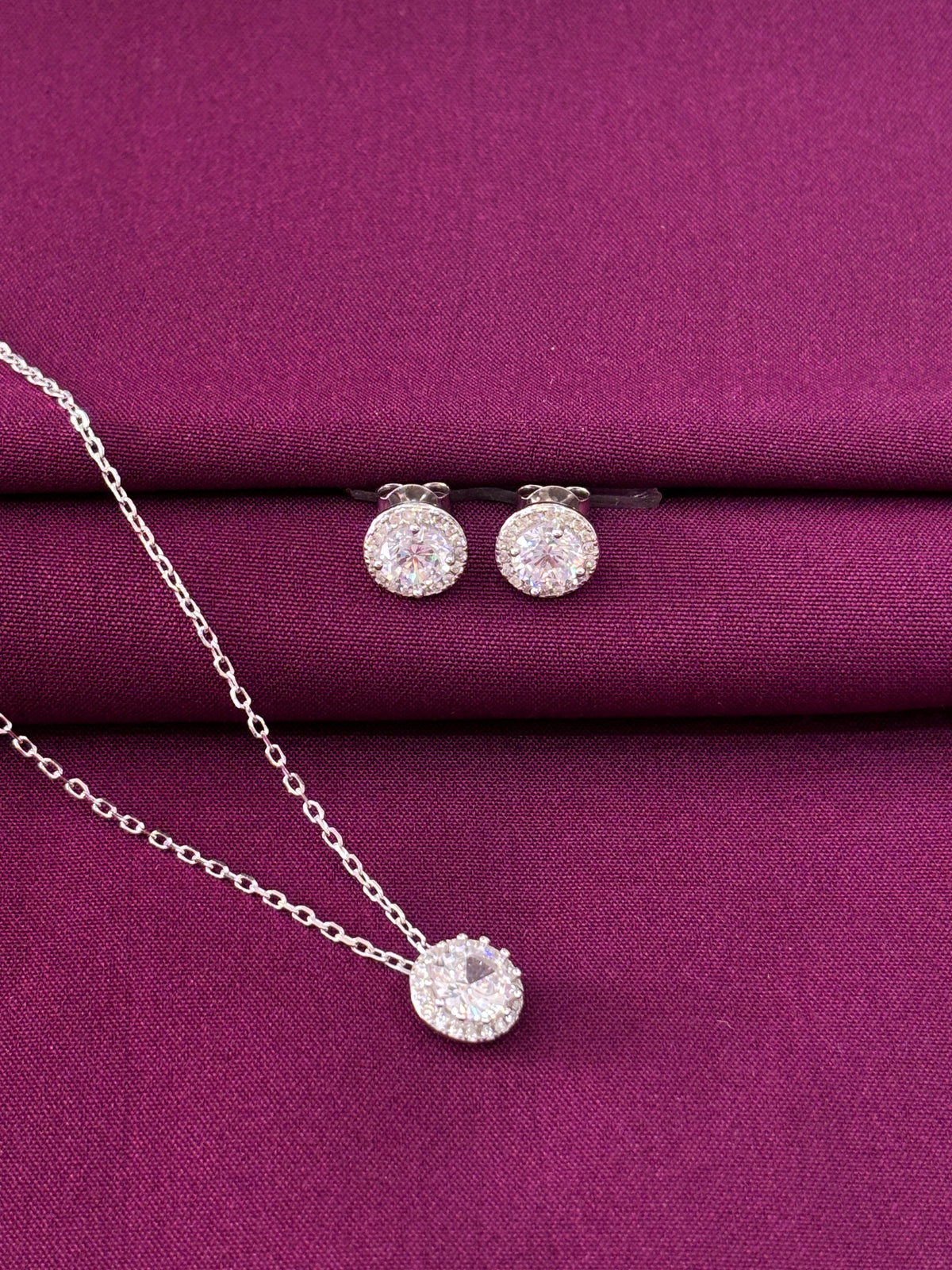 Silver jewelry set with earrings and a necklace on a purple fabric background