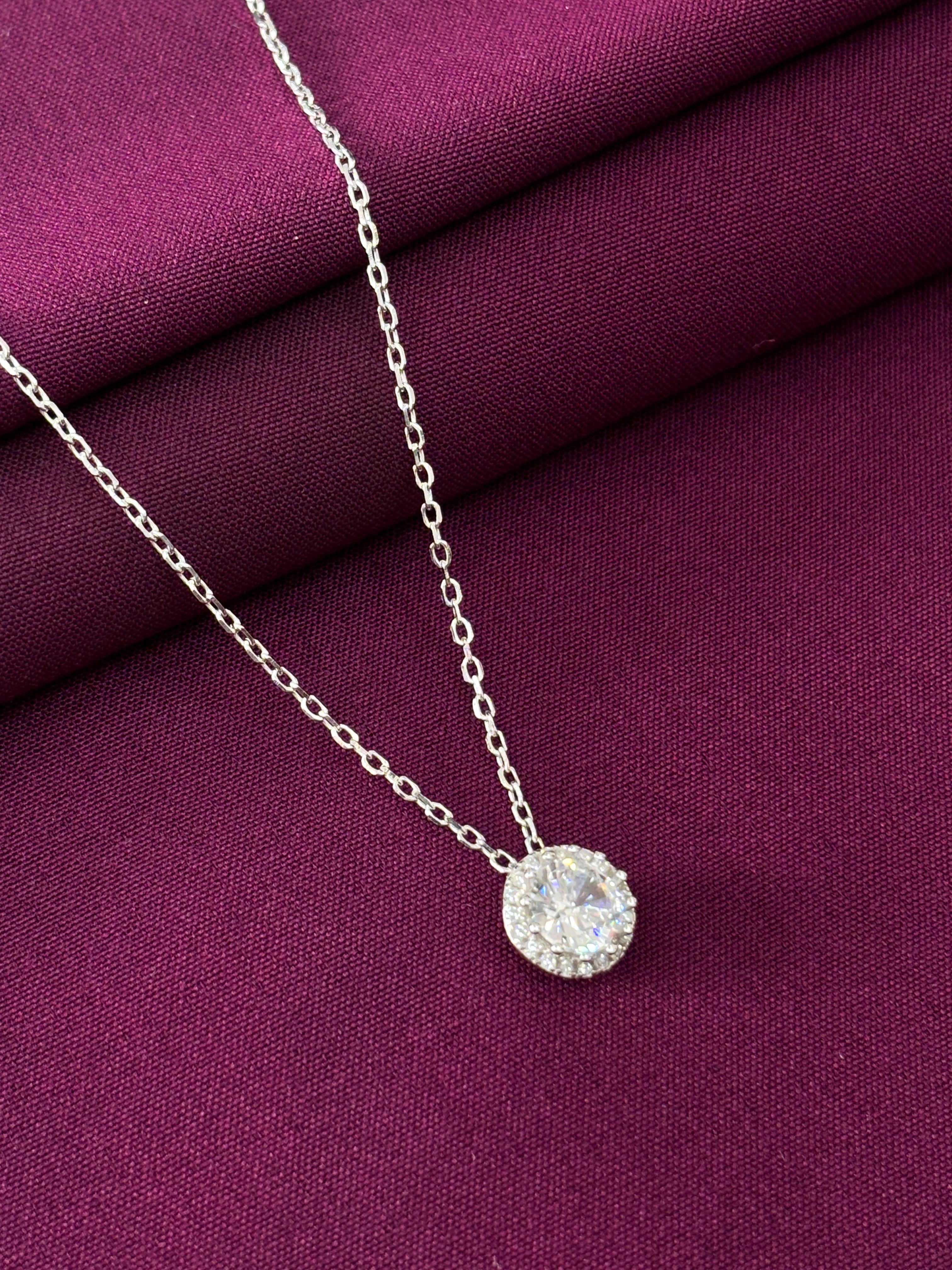 Silver necklace with a round pendant on a purple fabric background