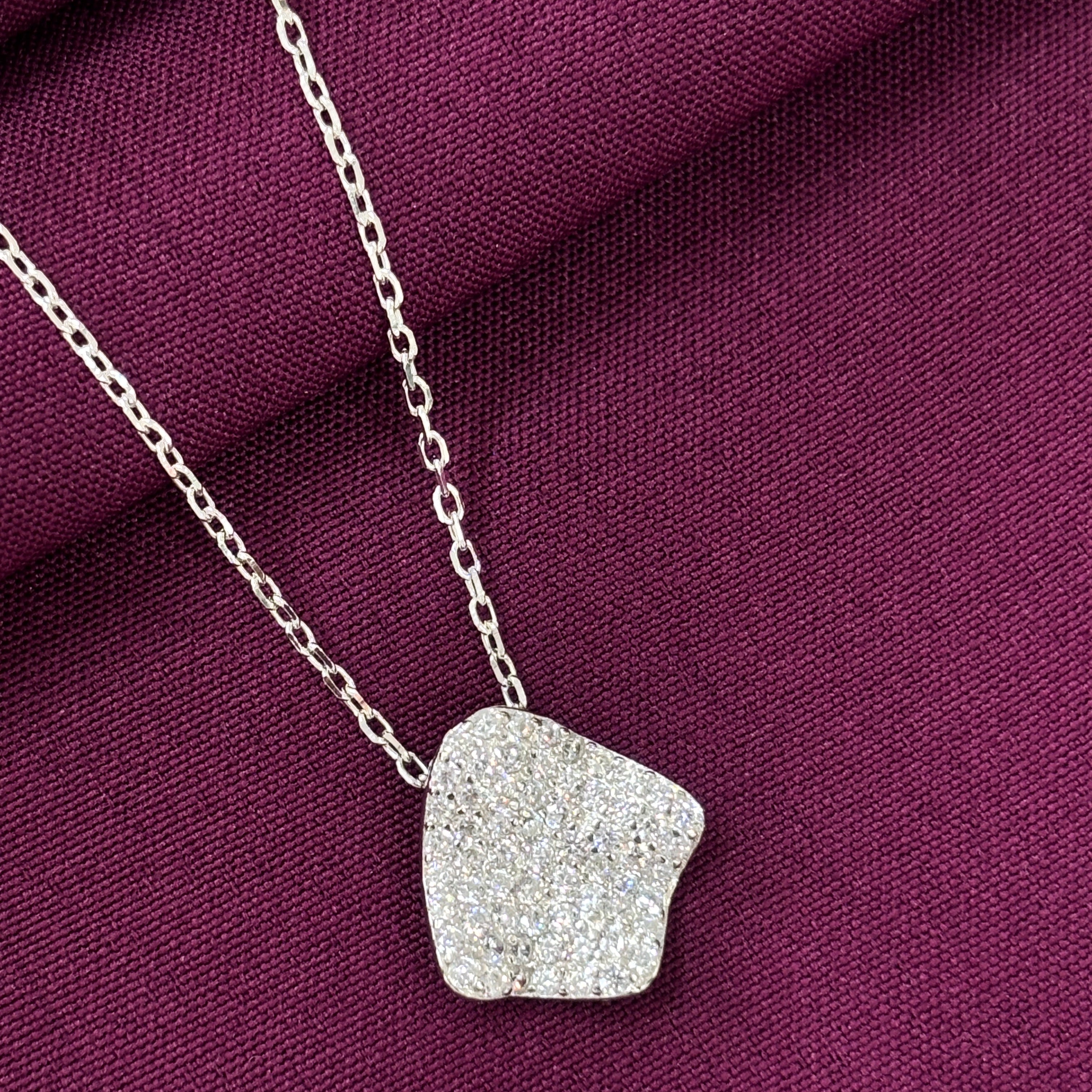 Silver necklace with a textured pendant on a purple fabric background
