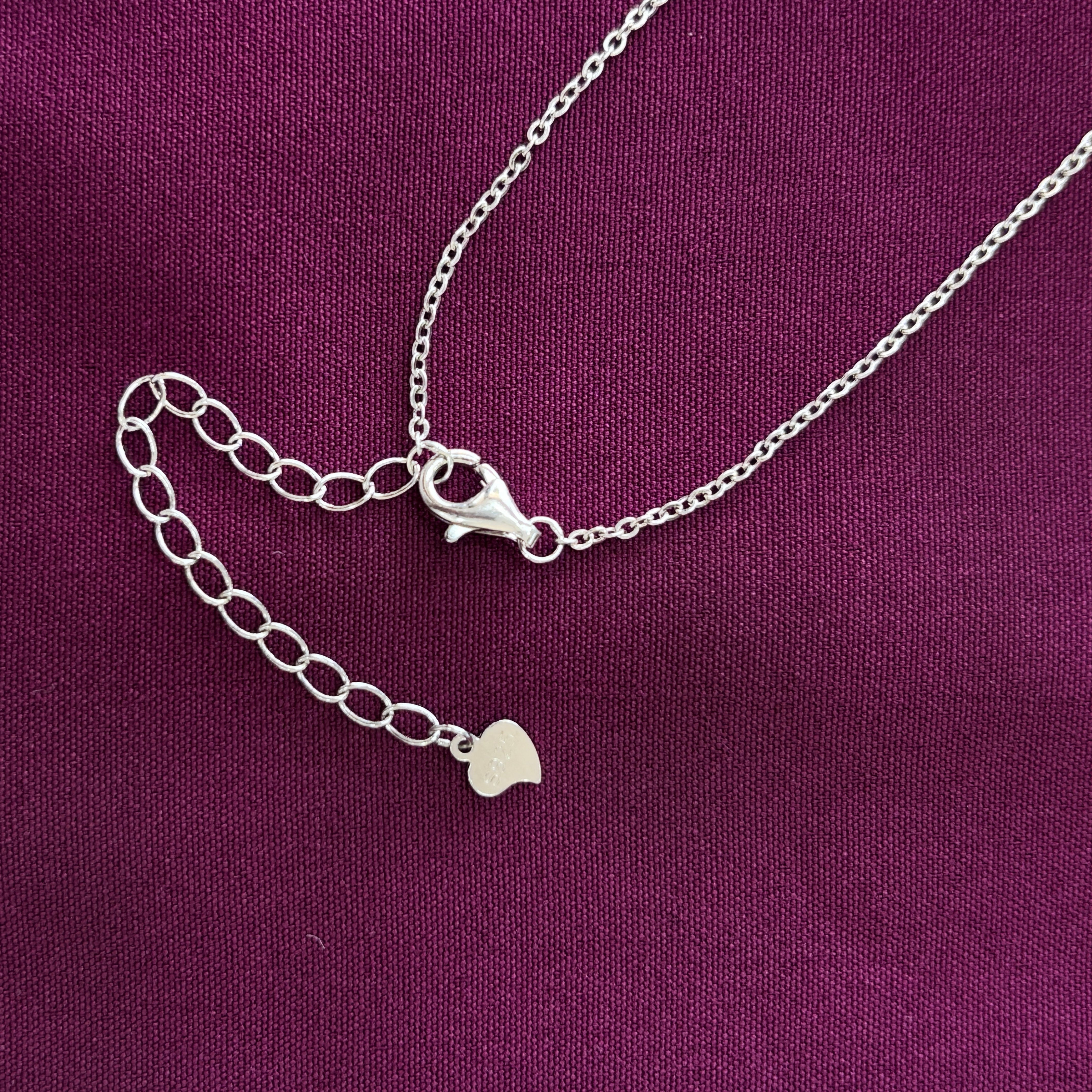 Silver necklace with heart charm on a purple fabric background