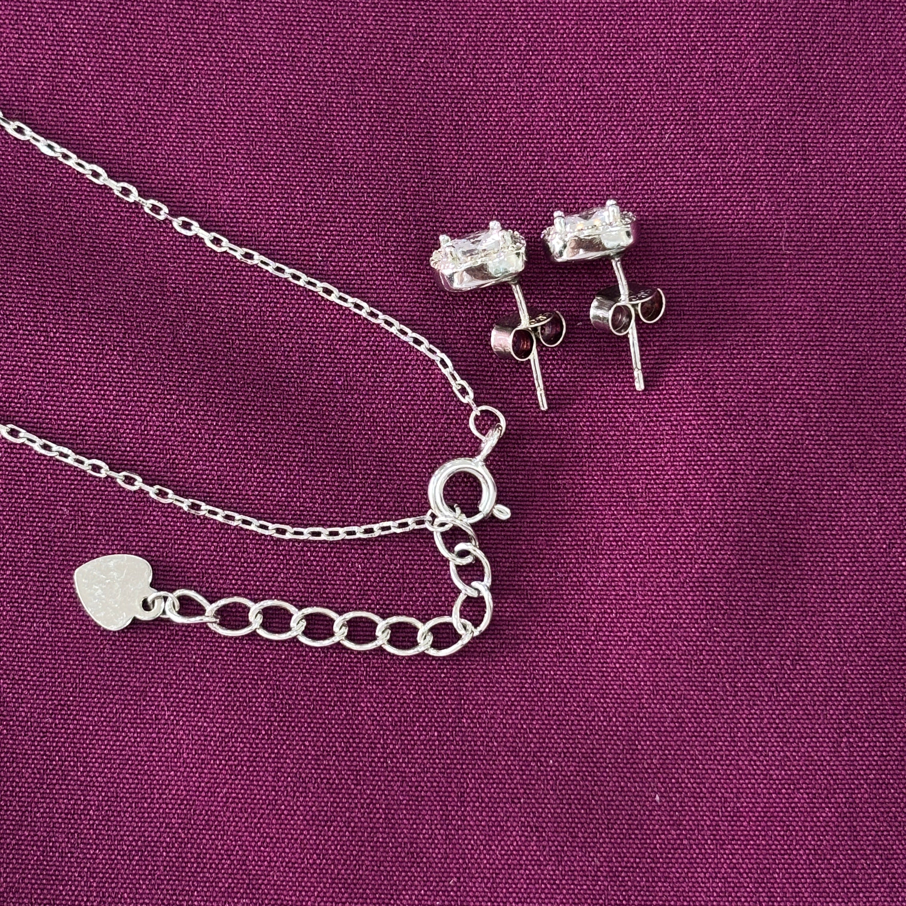 Silver necklace with heart charm and earrings on a purple fabric background