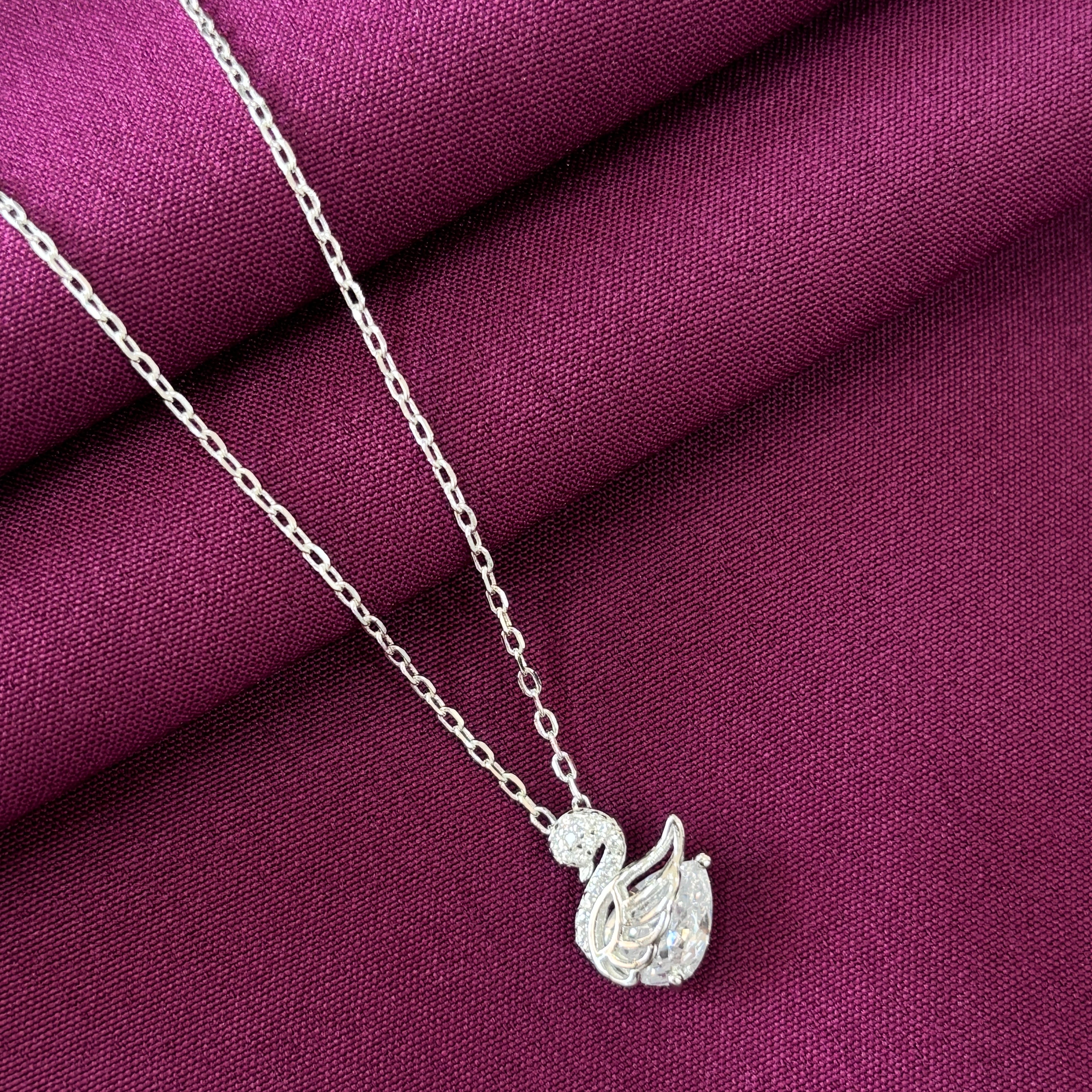 Silver necklace with a leaf pendant on a purple fabric background