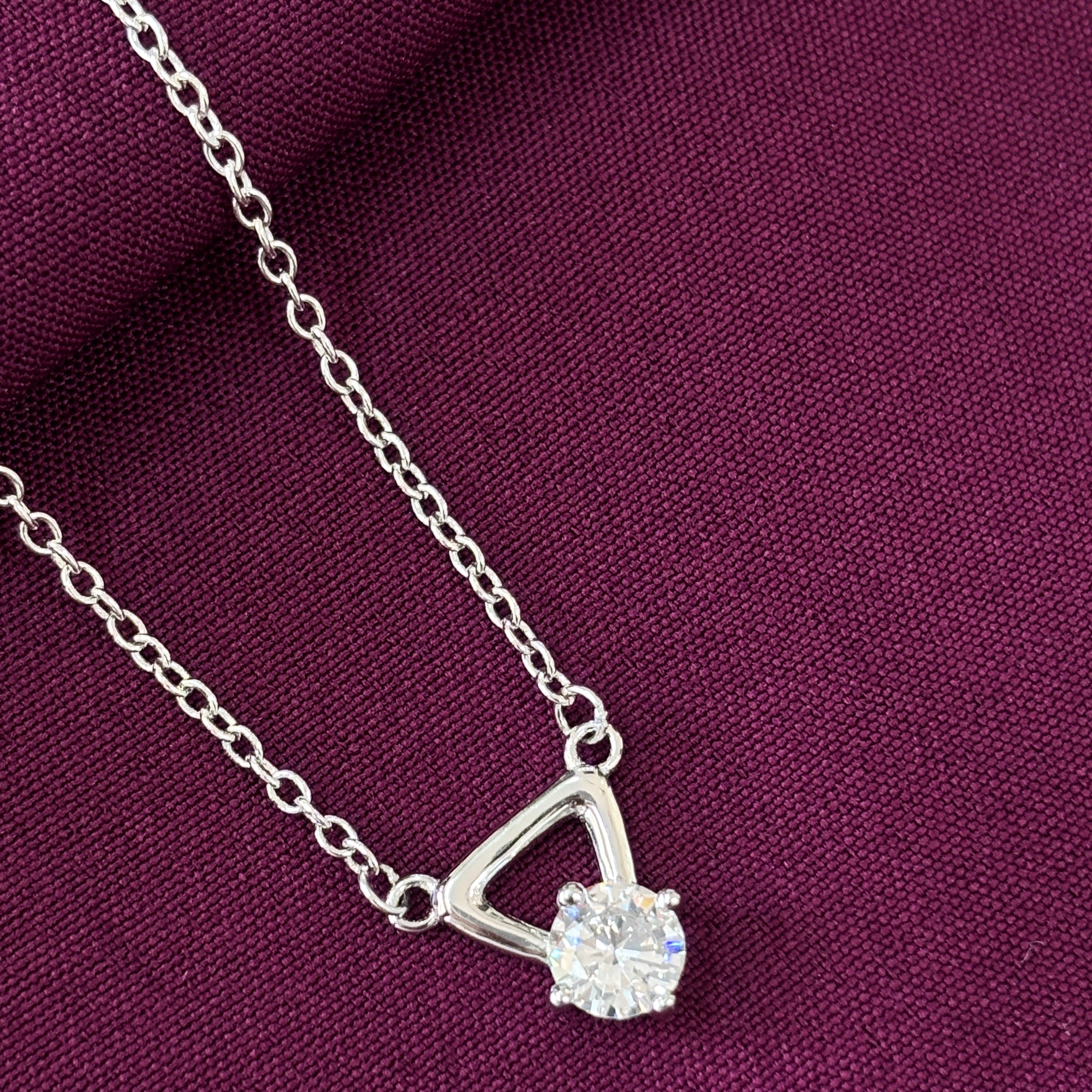 Silver necklace with a triangle pendant on a purple fabric background