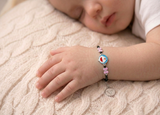 Child's hand wearing a colorful silver bracelet on a soft surface