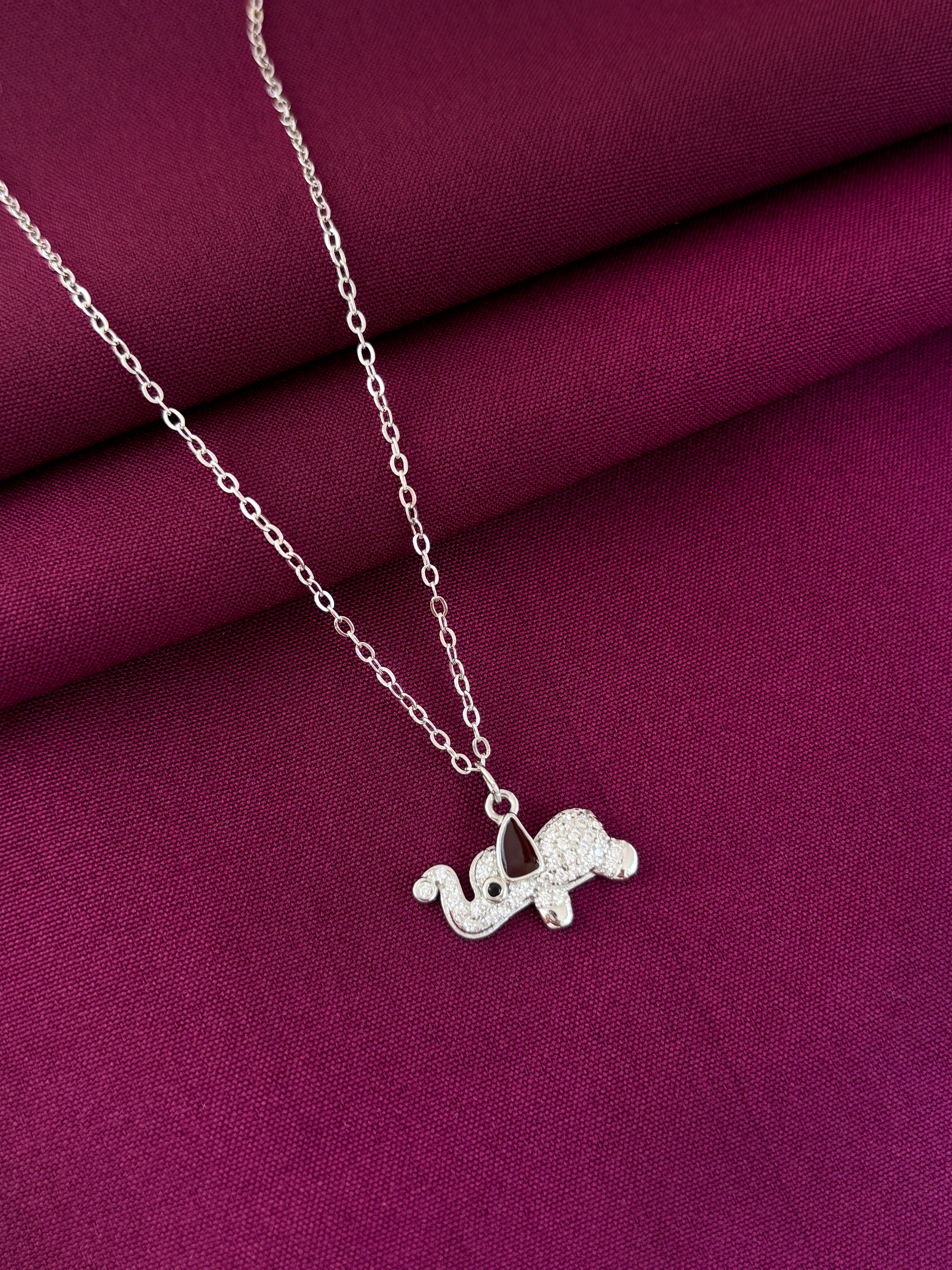 Silver necklace with a small elephant pendant on a purple fabric background